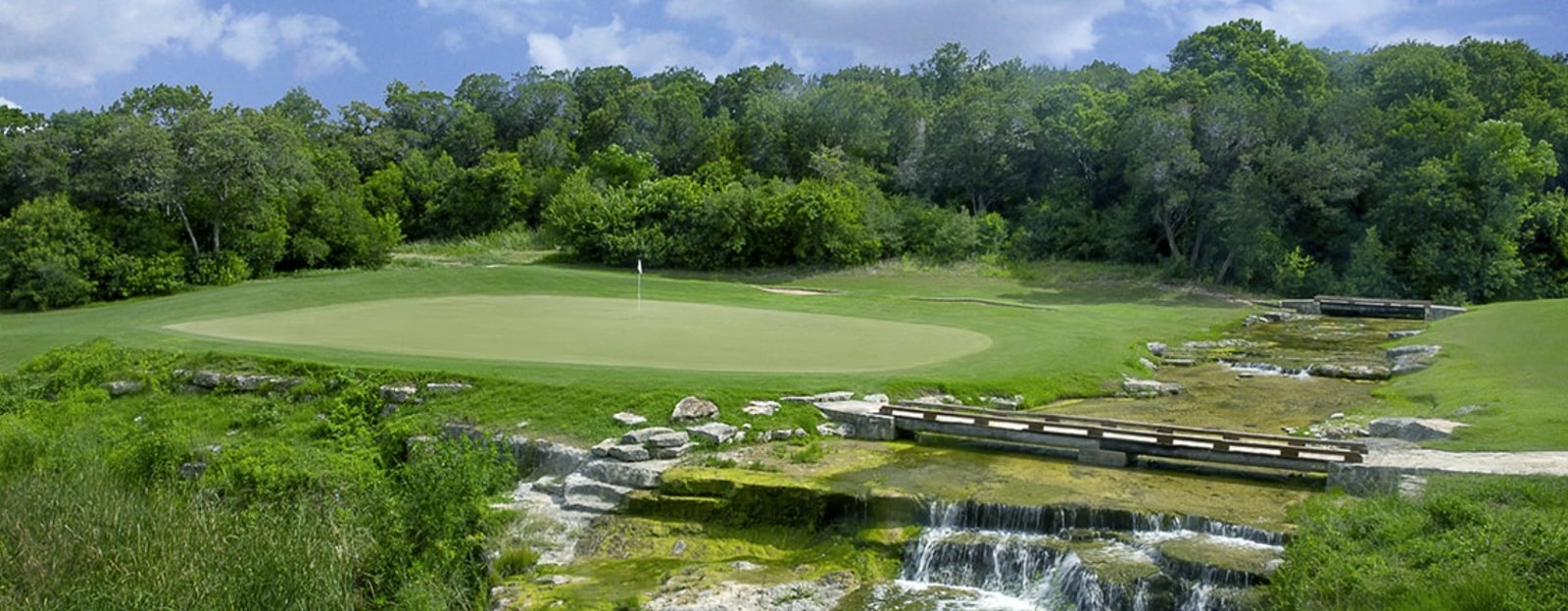 A green at Barton Creek Country Club in Austin, Texas, with a limestone creek and waterfall in the foreground
