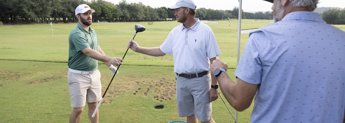 A Next Gear fitter handing a driver to a customer to test on the range