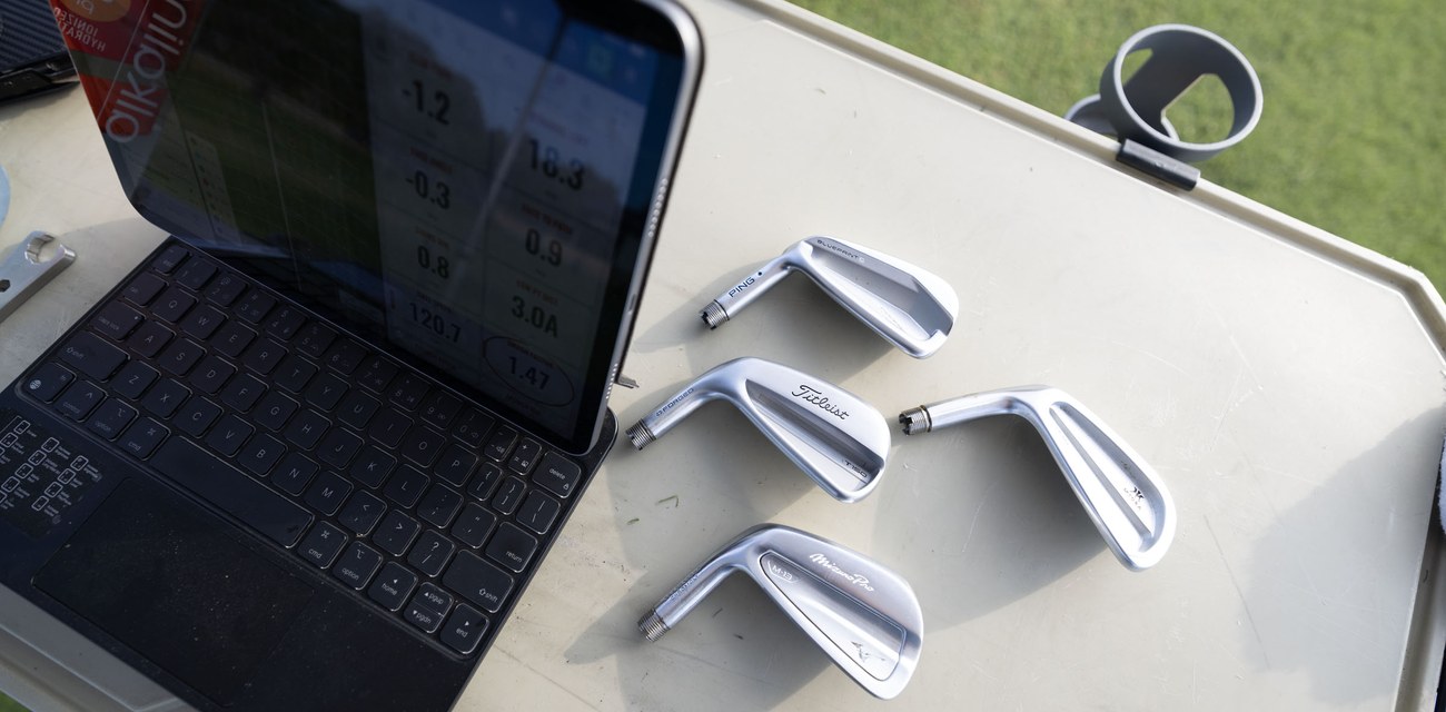 Launch monitor numbers on the fitting cart beside a row of bare iron heads ready to test